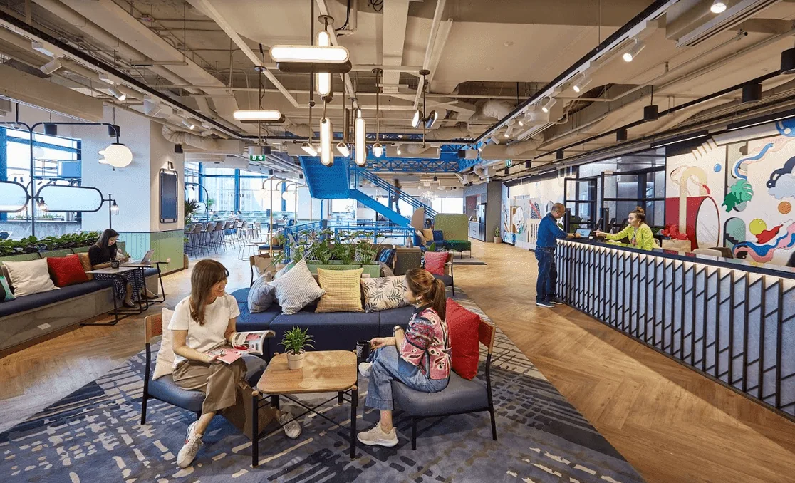 Open lounge inside JustCo Samyan Mitrtown with communal tables and neon signage