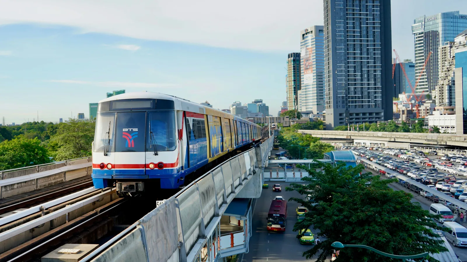 BTS Skytrain traveling on elevated tracks with Bangkok's modern skyline of glass and steel skyscrapers in the background