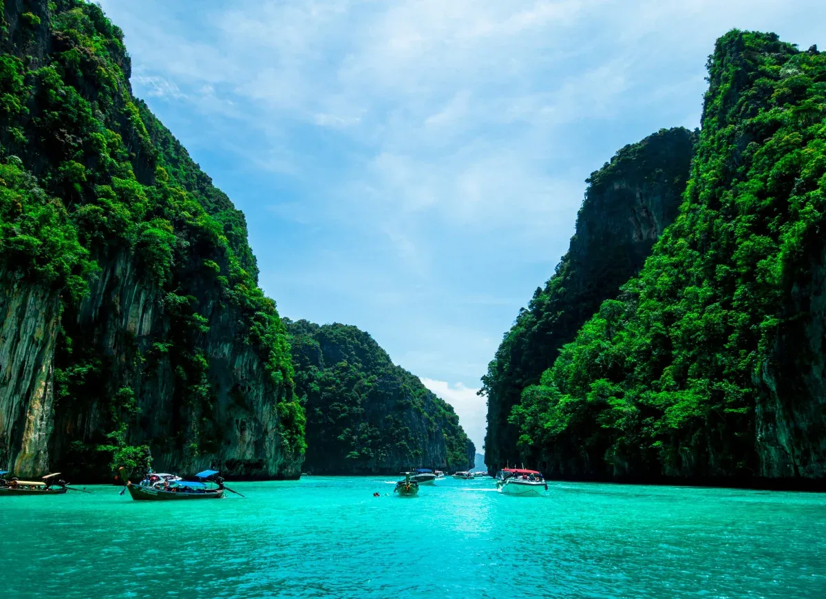 Iconic limestone karst cliffs rising from turquoise waters with longtail boats floating in crystal-clear Andaman Sea