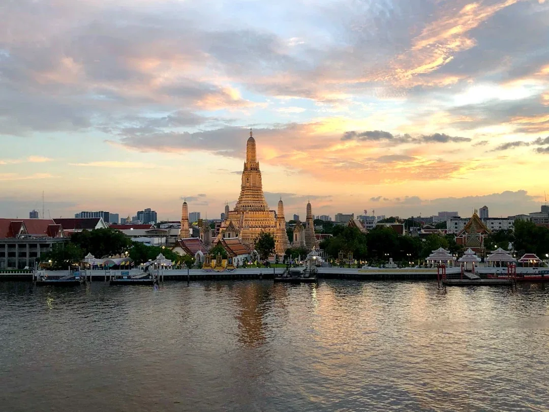Wat Arun temple illuminated at sunset, viewed across the Chao Phraya River in Bangkok, Thailand.