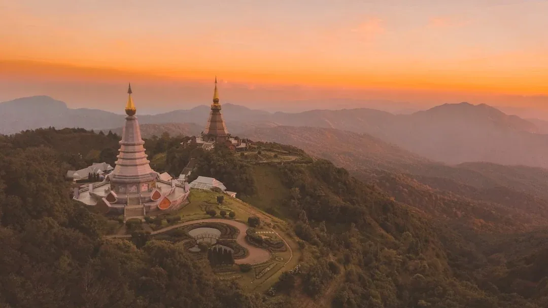 Aerial view of the twin royal chedis on Doi Inthanon, Chiang Mai, Thailand, at sunset, surrounded by mountains and forests.