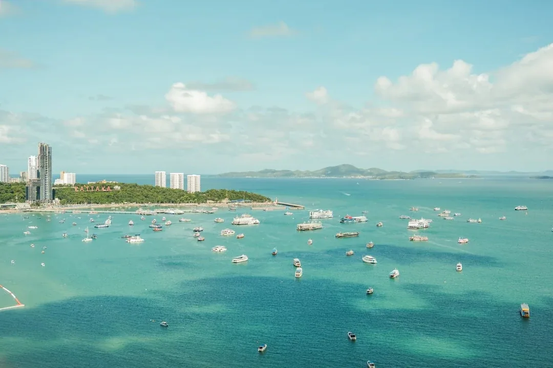 Aerial view of Pattaya Bay, Chon Buri, Thailand, with many boats on turquoise water, a city skyline, and distant islands.