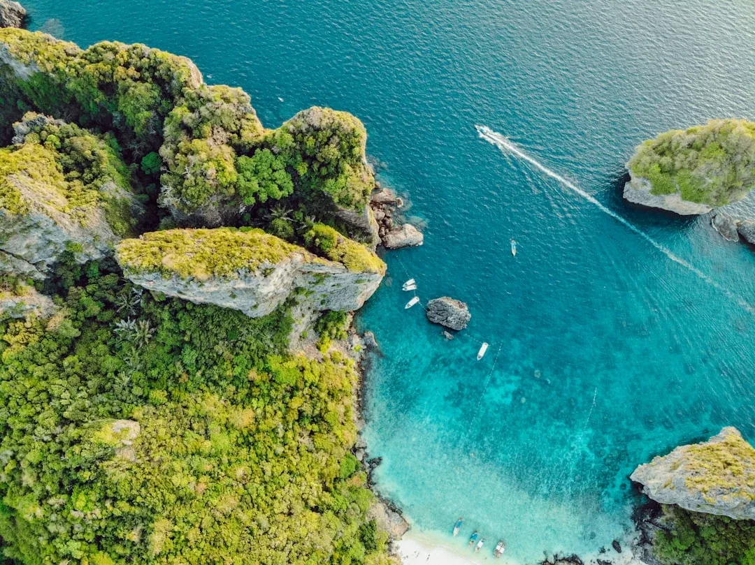 Aerial view of lush green limestone islands, a white sand beach, and turquoise waters with boats in Phi Phi Islands, Krabi, Thailand.