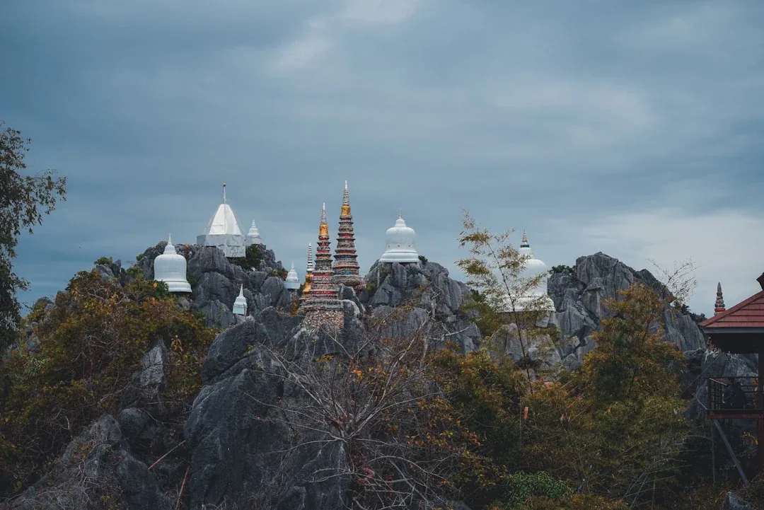 White and gold pagodas of Wat Chalermprakiat temple perched on jagged, rocky mountain peaks in Lampang, Thailand.
