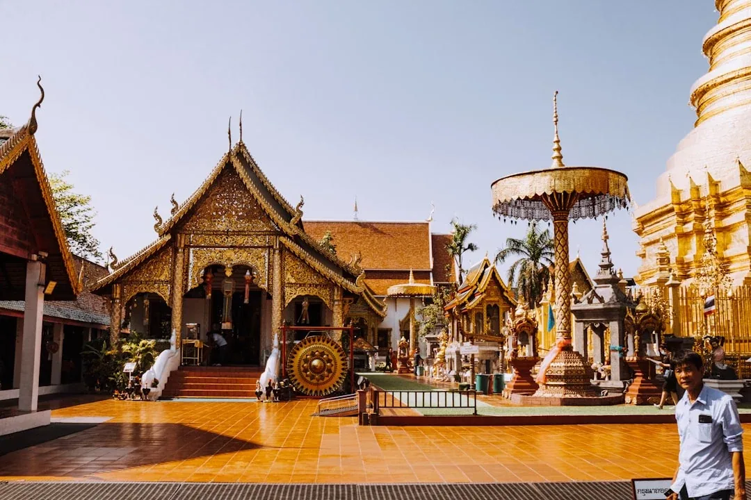 Wat Phra That Hariphunchai temple complex in Lamphun, Thailand, featuring ornate golden buildings, a large stupa, and a tiled courtyard under a bright sky.