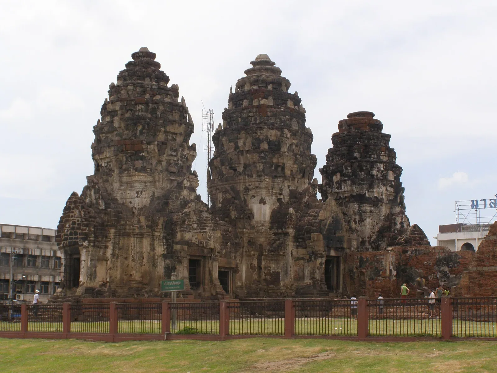 Phra Prang Sam Yot, an ancient Khmer-style temple with three weathered prangs, stands on a green lawn in Lopburi, Thailand.