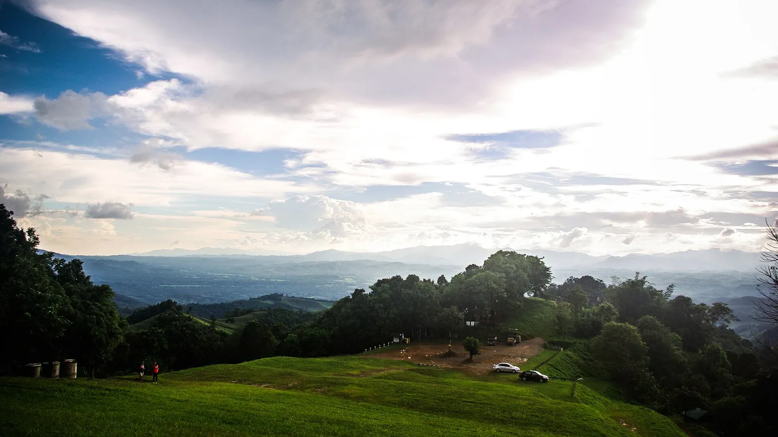 Panoramic view of Doi Samoe Dao in Nan province, showing rolling green hills, distant mountains, and a cloudy sky.