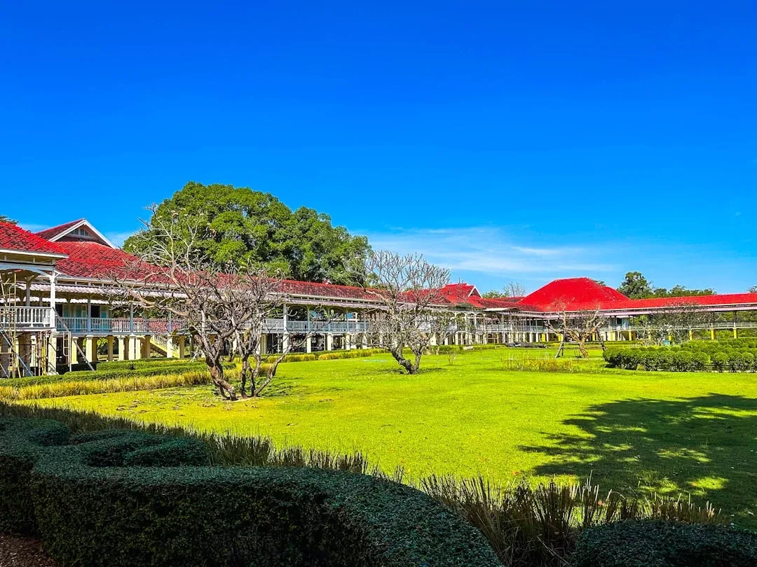 Phra Ram Ratchaniwet Palace (Wang Ban Puen) in Phetchaburi, a long white building with red roofs and balconies, surrounded by a green lawn under a clear blue sky.