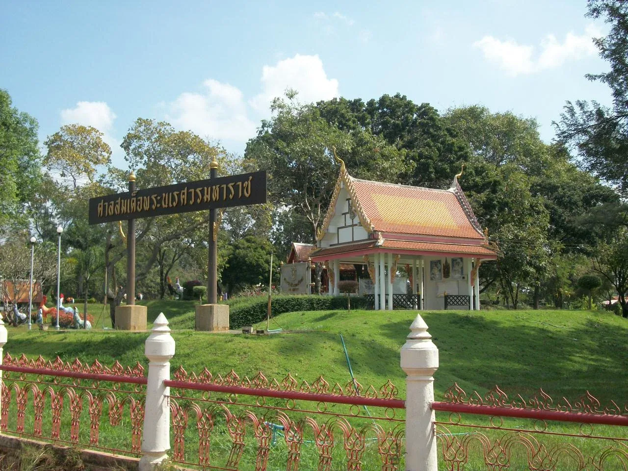 The Shrine of King Naresuan, a traditional Thai building with an orange roof, on a green hill with a sign in Thai script, surrounded by trees.