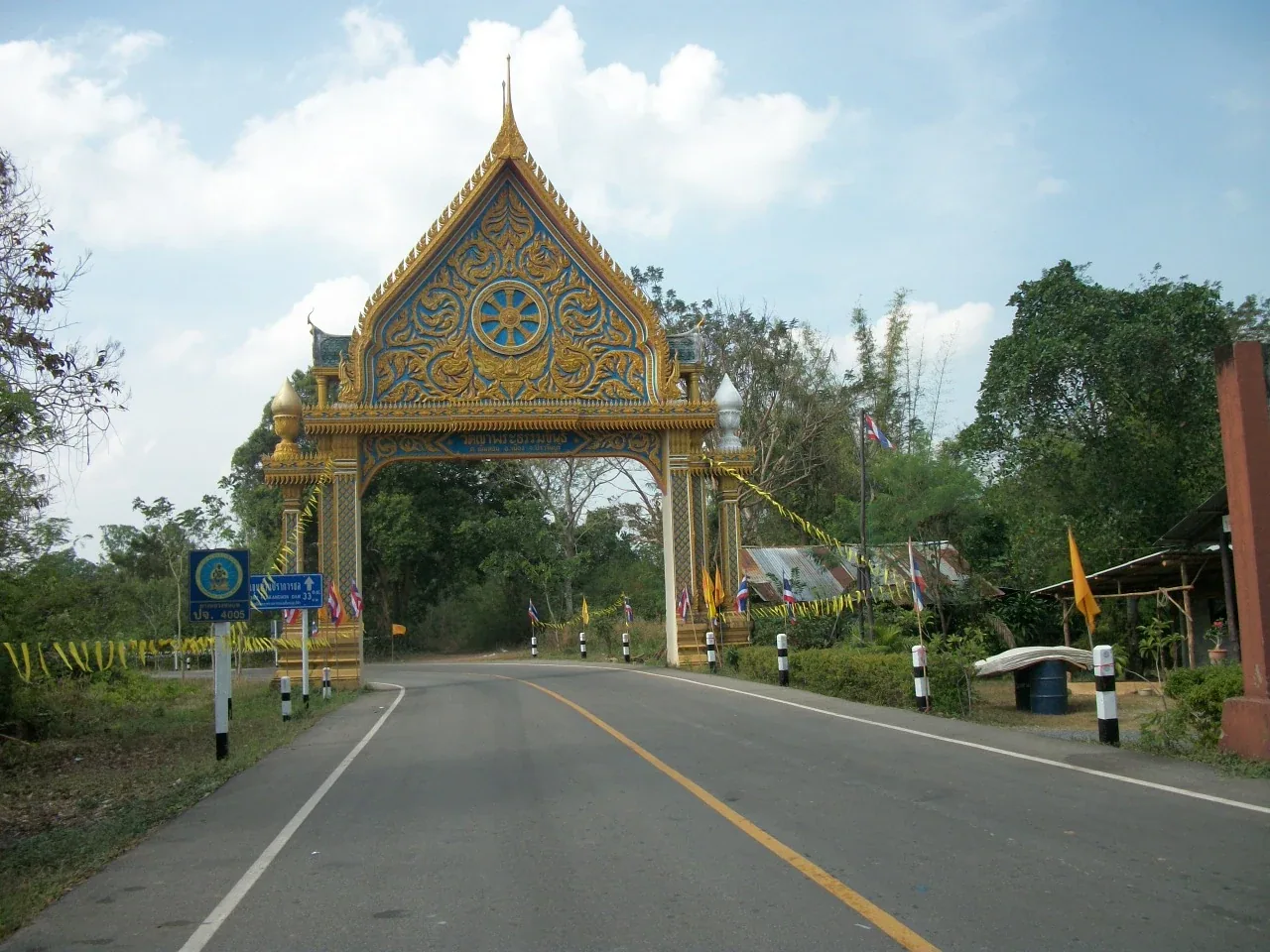 Ornate golden and blue temple gate of Wat Phratumkhan spanning a road in Prachin Buri, Thailand.