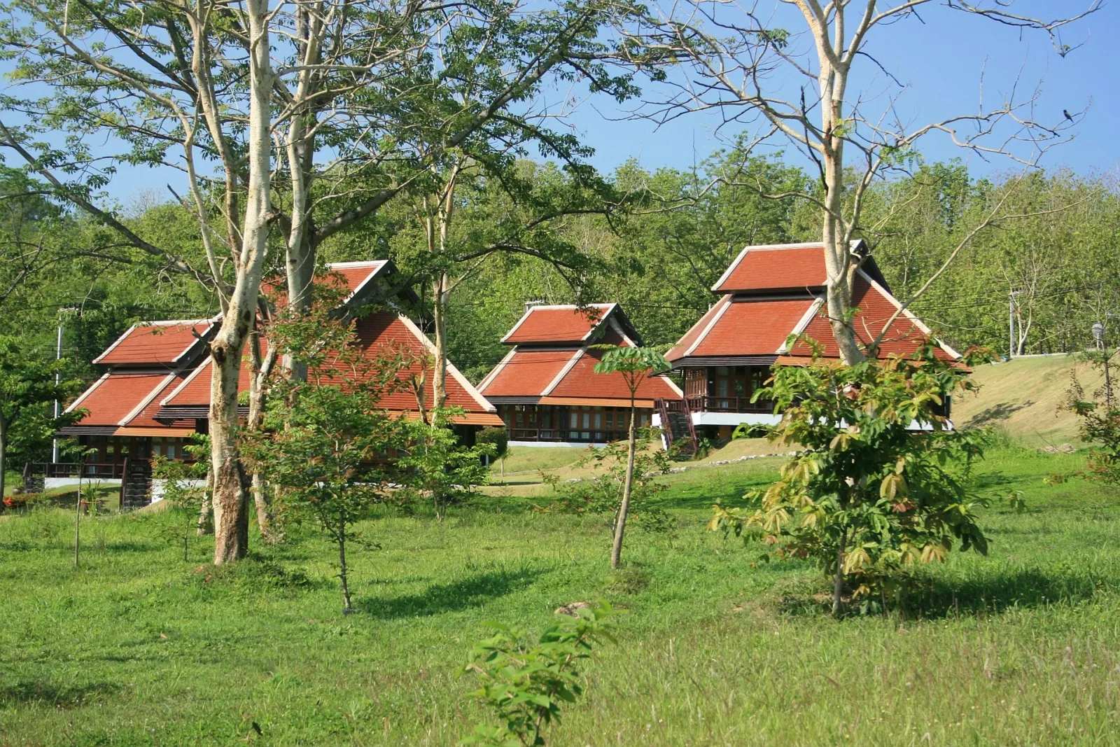 Three traditional Thai-style buildings with red tiered roofs surrounded by green grass and trees at Chet Khot-Pong Kon Sao Nature Study Centre.